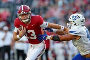 The cover for this College football picks week 14 article shows John Gazzaniga #13 of the Alabama Crimson Tide giving a stiff arm to Jesse Garza #49 of the Eastern Illinois Panthers.