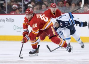 The cover for this NHL parlay picks today article shows Blake Coleman #20 of the Calgary Flames protects the puck from Gustav Nyquist #14 of the Winnipeg Jets.