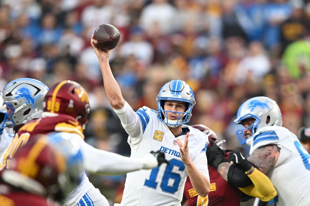 The cover for this Sunday night football picks article shows Jared Goff #16 of the Detroit Lions looking to pass against the Washington Commanders