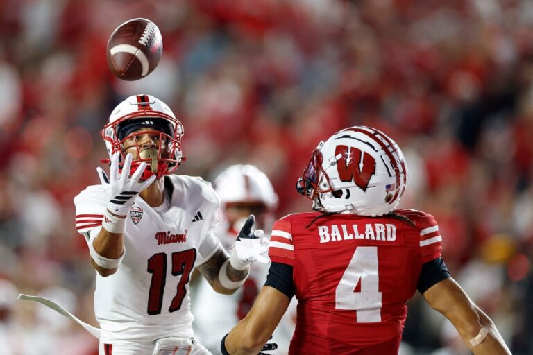 The cover for this Wednesday night college football picks article shows Kaleb Martin #17 of the Miami (OH) Redhawks breaking up a pass intended for Jayden Ballard #4 of the Wisconsin Badgers