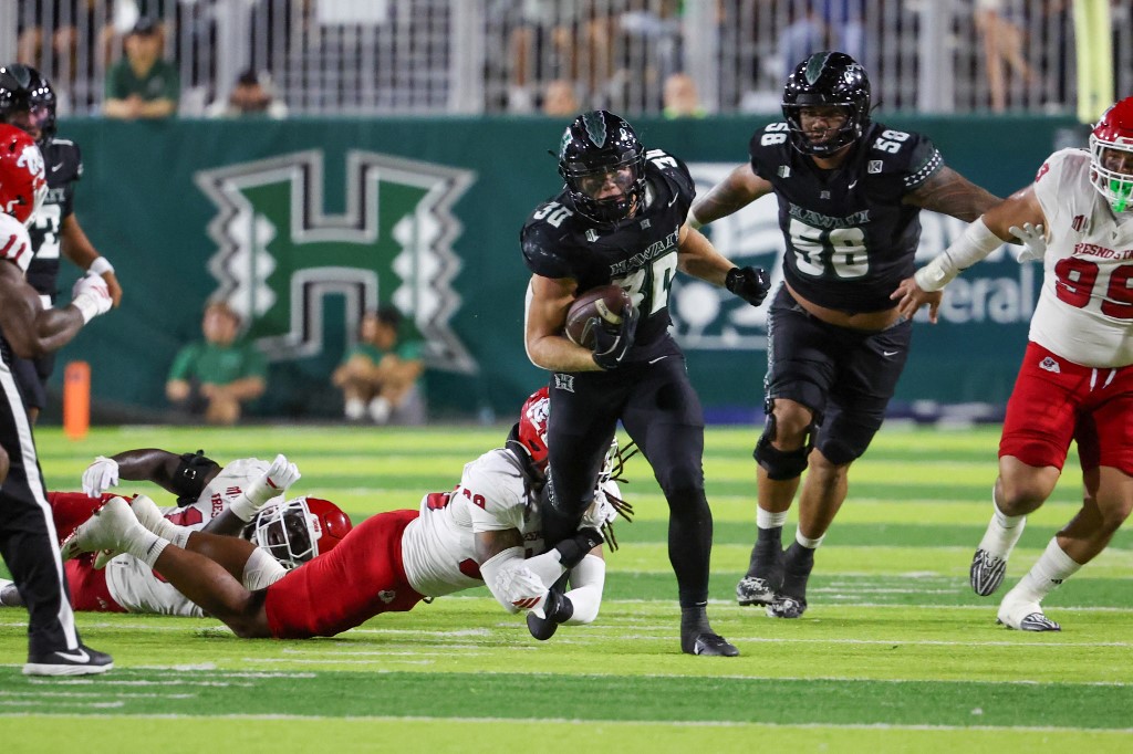 The cover for this Friday night college football picks article shows Landon Sims #30 of the Hawaii Rainbow Warriors breaking free from Jadon Pearson #39 of the Fresno State Bulldogs.