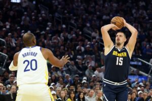 The cover for this NBA player props today article shows Nikola Jokic #15 of the Denver Nuggets shooting over Al Horford #20 of the Golden State Warriors