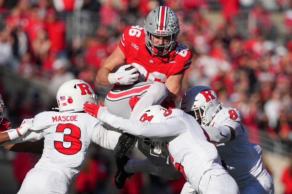 The cover for this College football odds week 14 article shows tight end Max Klare #86 of the Ohio State Buckeyes jumping over Defensive back Bo Mascoe #3, Defensive back Kaj Sanders #5 and Linebacker Dariel Djabome #8 of the Rutgers Scarlet Knights while carrying the ball.