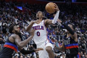 The cover for this NBA picks today article shows Tyrese Maxey #0 of the Philadelphia 76ers going to the basket between Paul Reed #7 and Daniss Jenkins #24 of the Detroit Pistons.