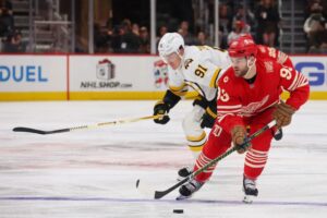 The cover for this NHL picks today article shows Alex Debrincat #93 of the Detroit Red Wings skating with the puck in front of Nikita Zadorov #91 of the Boston Bruins.