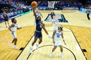 The cover for this college basketball picks today article shows Deyton Albury #13 of the Utah State Aggies attempting a layup while being guarded by Kobe Johnson #0 of the UCLA Bruins.