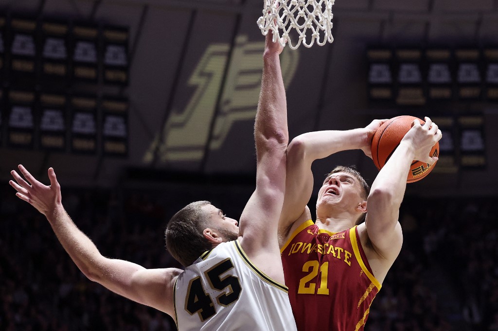 The cover for this college basketball picks article shows Dominykas Pleta #21 of the Iowa State Cyclones shooting over Oscar Cluff #45 of the Purdue Boilermakers.