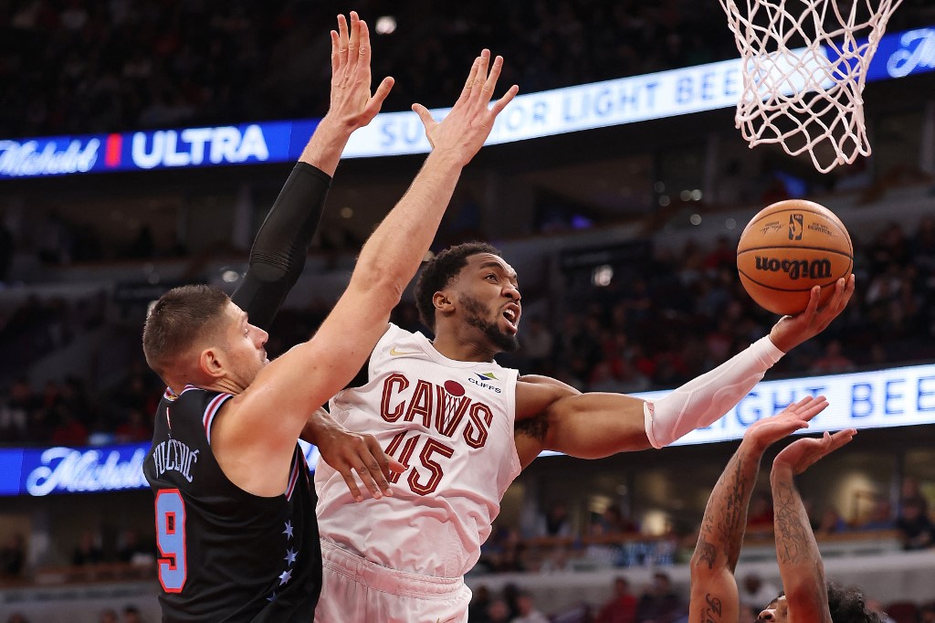 The cover for this NBA player props today article shows Donovan Mitchell #45 of the Cleveland Cavaliers going up for a layup against Nikola Vucevic #9 and Coby White #0 of the Chicago Bulls.
