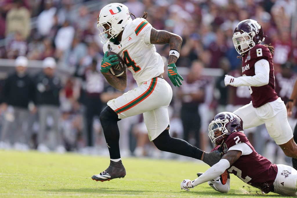 The cover for this college football odds today article shows Mark Fletcher Jr. #4 of the Miami Hurricanes runs the ball against Dezz Ricks #2 of the Texas A&M Aggies.