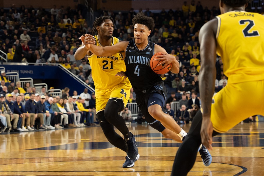 The cover for this college basketball picks today article shows Tyler Perkins #4 of the Villanova Wildcats going to the basket against Morez Johnson Jr. #21 of the Michigan Wolverines.