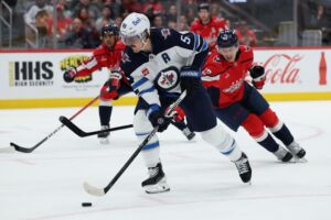 Mark Scheifele #55 of the Winnipeg Jets skates past Martin Fehérváry #42 of the Washington Capitals.