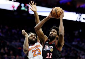 New York Knicks v Philadelphia 76ers - Oddstrader The cover for this NBA player props today article shows Joel Embiid #21 of the Philadelphia 76ers driving to the basket against Mitchell Robinson #23 of the New York Knicks.