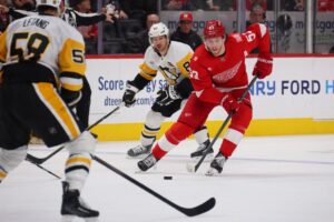 The cover for this NHL picks today article shows Moritz Seider #53 of the Detroit Red Wings controlling the puck in front of Sidney Crosby #87 of the Pittsburgh Penguins.