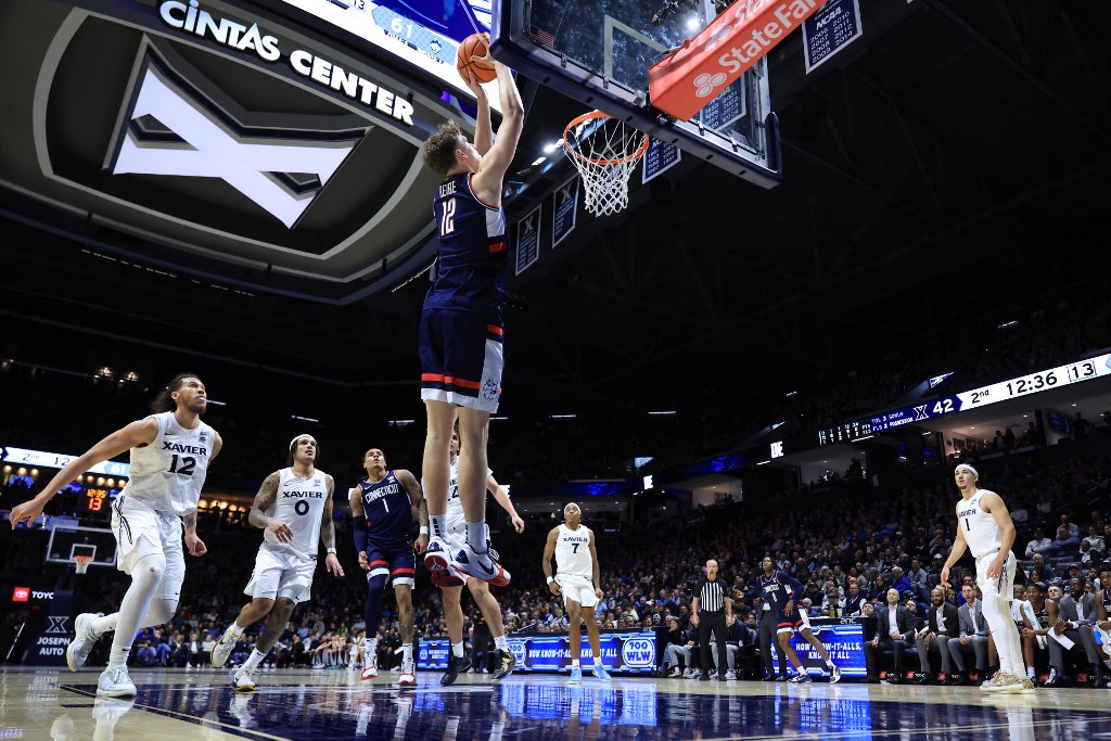 The cover for this college basketball picks today article shows Eric Reibe #12 of the UConn Huskies dunking the ball against the Xavier Musketeers during the second half.